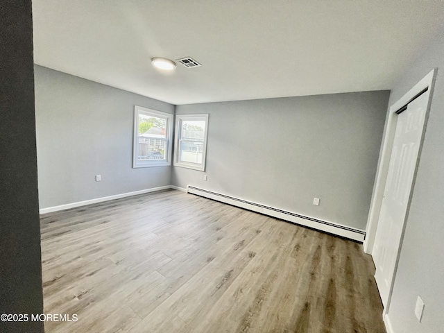 unfurnished bedroom featuring a baseboard heating unit, wood finished floors, baseboards, and a closet