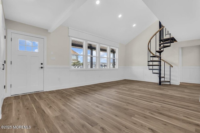 foyer with wood finished floors, a wainscoted wall, stairway, a decorative wall, and vaulted ceiling