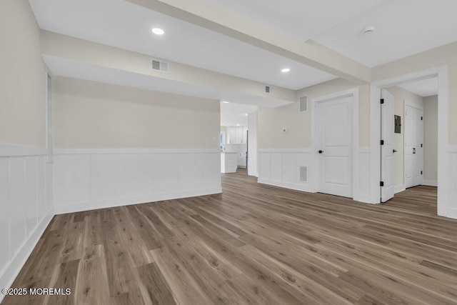spare room with a decorative wall, a wainscoted wall, visible vents, and wood finished floors