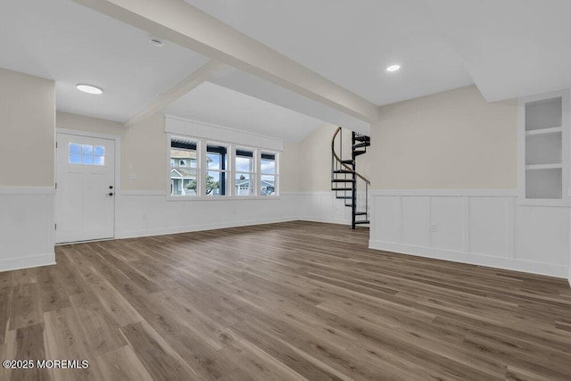 unfurnished living room with stairway, a decorative wall, a wainscoted wall, and wood finished floors