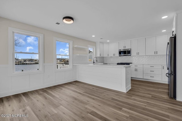kitchen featuring visible vents, white cabinetry, a peninsula, wood finished floors, and appliances with stainless steel finishes