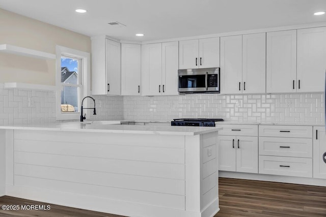 kitchen featuring a sink, stainless steel microwave, white cabinetry, a peninsula, and dark wood-type flooring