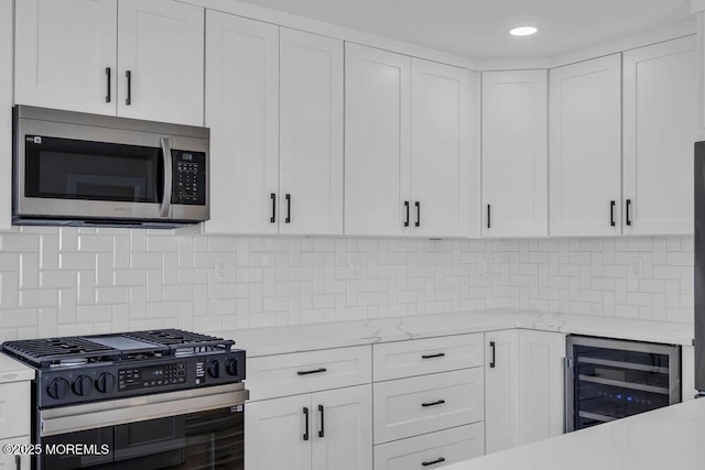 kitchen featuring beverage cooler, white cabinets, light stone countertops, appliances with stainless steel finishes, and decorative backsplash