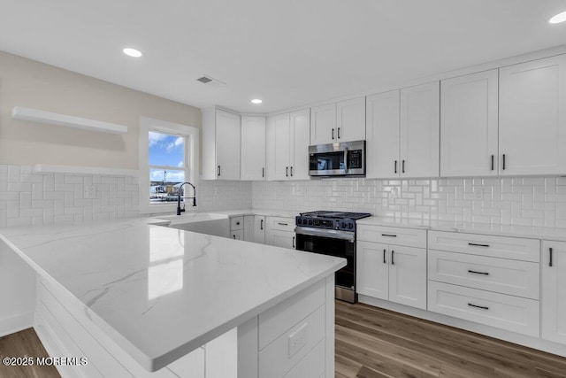 kitchen featuring a peninsula, a sink, open shelves, white cabinetry, and appliances with stainless steel finishes