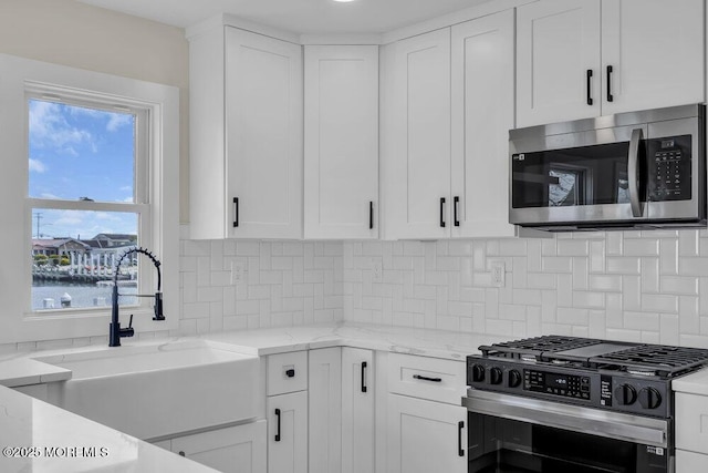 kitchen with a sink, stainless steel appliances, light stone counters, decorative backsplash, and white cabinets