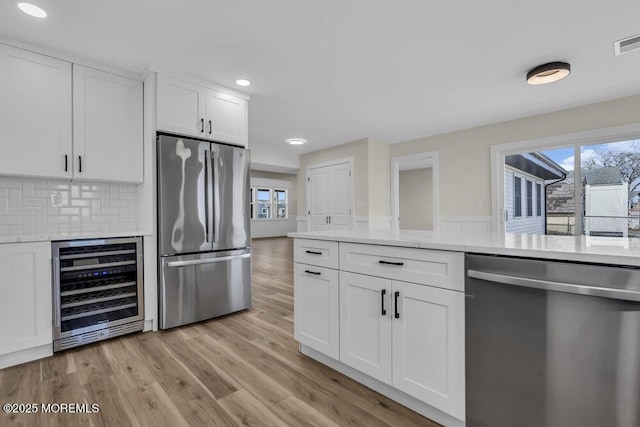 kitchen with recessed lighting, beverage cooler, stainless steel appliances, white cabinets, and light wood-type flooring