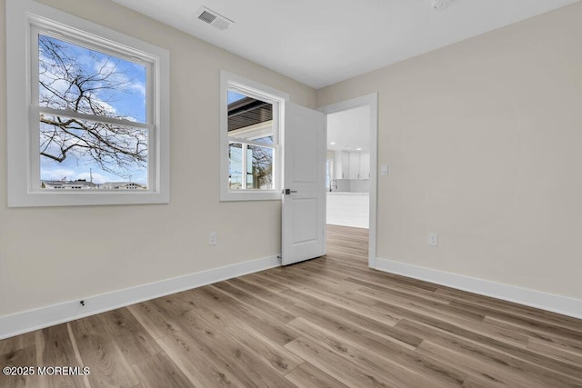 spare room featuring light wood-style floors, visible vents, and baseboards