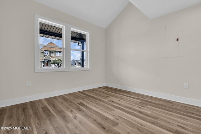 unfurnished room with baseboards, lofted ceiling, electric panel, and wood finished floors