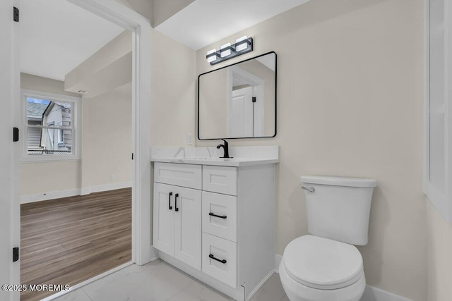 half bathroom featuring toilet, baseboards, and vanity