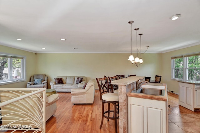 living area featuring light wood finished floors, crown molding, a wealth of natural light, and a notable chandelier