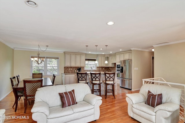 living room with plenty of natural light, a chandelier, ornamental molding, and light wood-style floors
