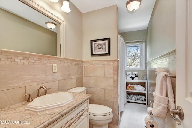 bathroom with toilet, tile walls, vanity, and a wainscoted wall