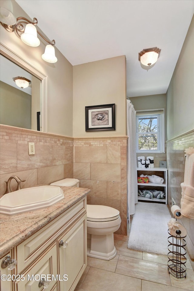 full bathroom featuring tile walls, toilet, a wainscoted wall, vanity, and tile patterned flooring