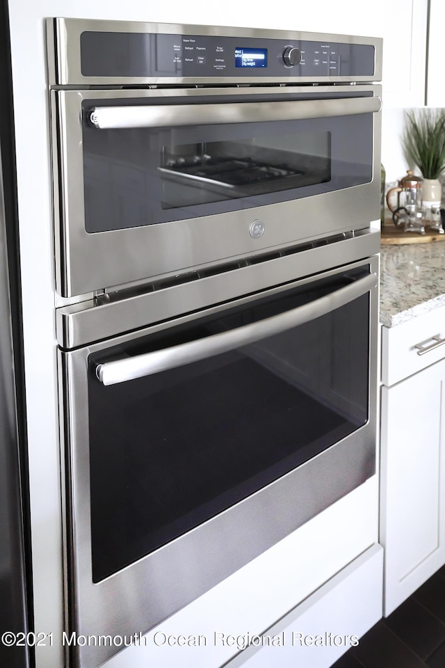 room details with white cabinets, decorative backsplash, light stone counters, and stainless steel double oven