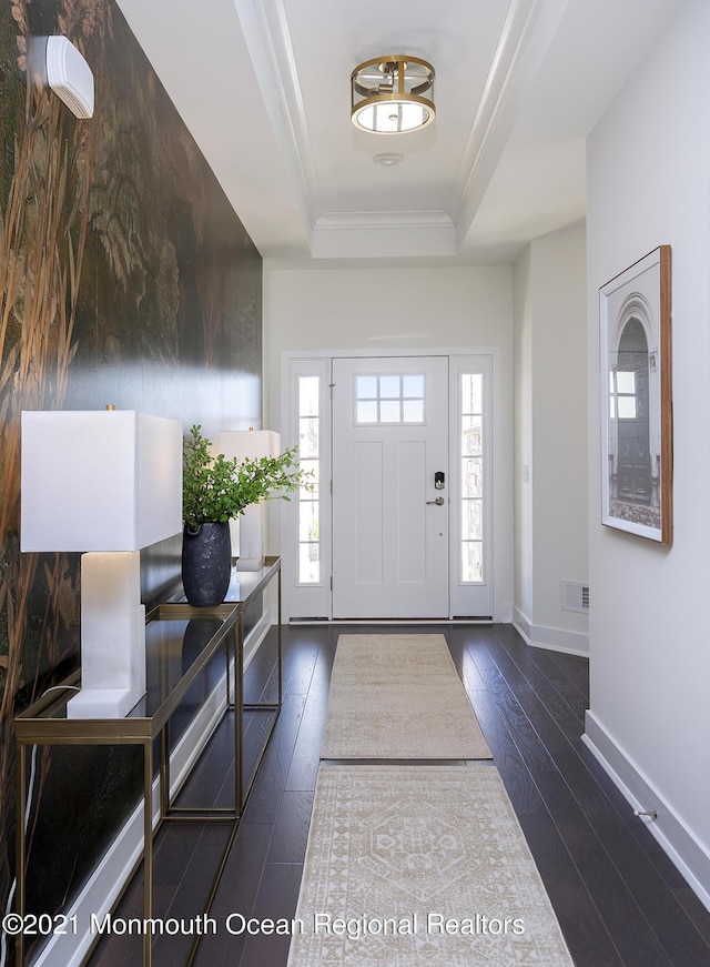 foyer featuring a tray ceiling, baseboards, visible vents, crown molding, and dark wood-type flooring
