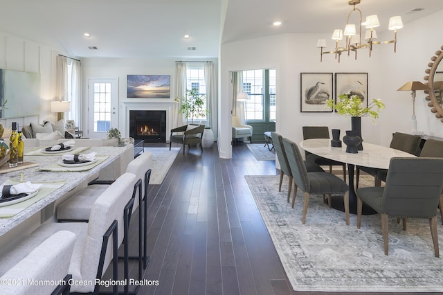 dining area featuring a warm lit fireplace, visible vents, recessed lighting, dark wood-style flooring, and a notable chandelier