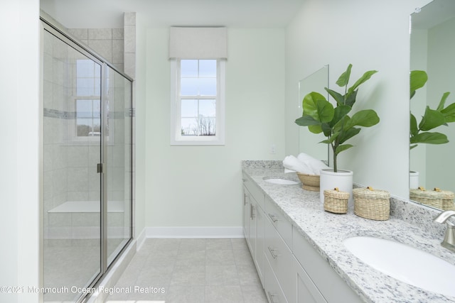 bathroom with a sink, a stall shower, double vanity, and baseboards
