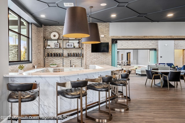 kitchen featuring a kitchen bar, brick wall, visible vents, and wood finished floors