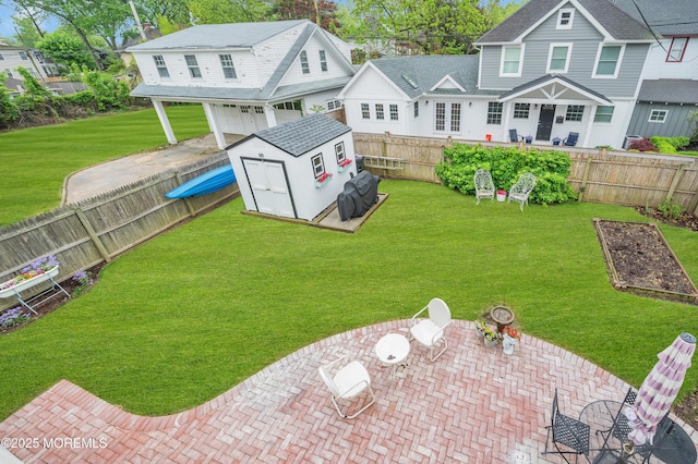 rear view of house with a patio, a storage unit, an outbuilding, an attached garage, and a garden