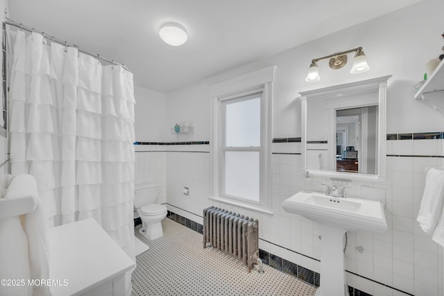 bathroom with radiator, tile walls, toilet, wainscoting, and a shower with curtain
