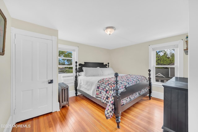 bedroom featuring radiator, multiple windows, light wood-style floors, and baseboards