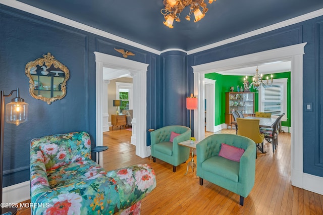 sitting room with a chandelier, wood-type flooring, ornamental molding, and baseboards