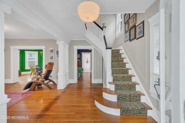 foyer with ornate columns, light wood-style floors, stairway, ornamental molding, and baseboards