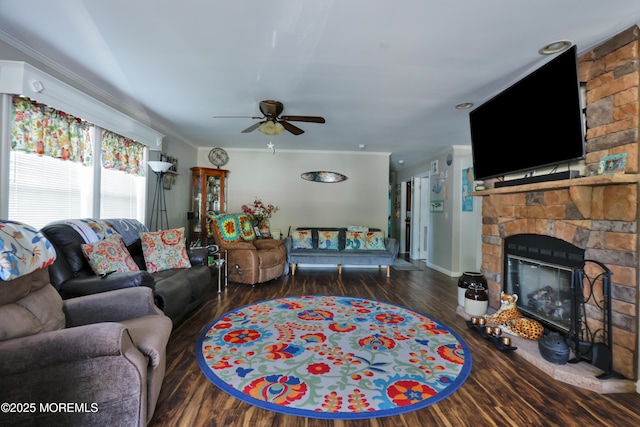 living room with ornamental molding, ceiling fan, wood finished floors, a stone fireplace, and baseboards