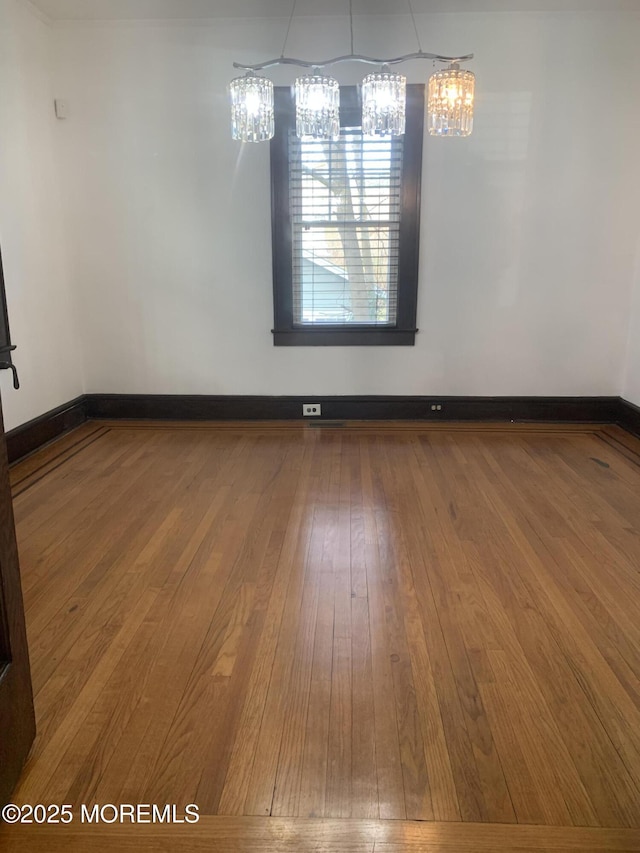spare room with hardwood / wood-style flooring, baseboards, and a chandelier