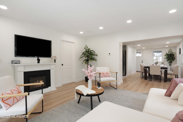 living room featuring baseboards, light wood finished floors, a glass covered fireplace, and recessed lighting