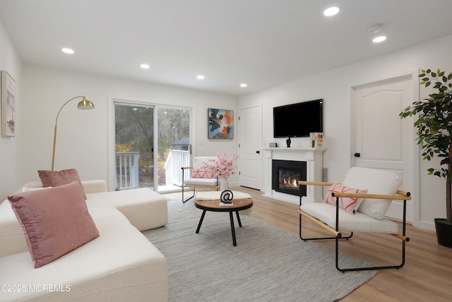 living room with recessed lighting, light wood-type flooring, and a glass covered fireplace