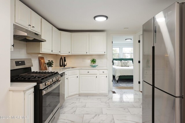 kitchen featuring white cabinetry, under cabinet range hood, light countertops, appliances with stainless steel finishes, and marble finish floor