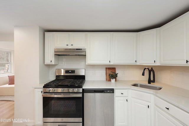 kitchen with a sink, under cabinet range hood, white cabinetry, backsplash, and appliances with stainless steel finishes