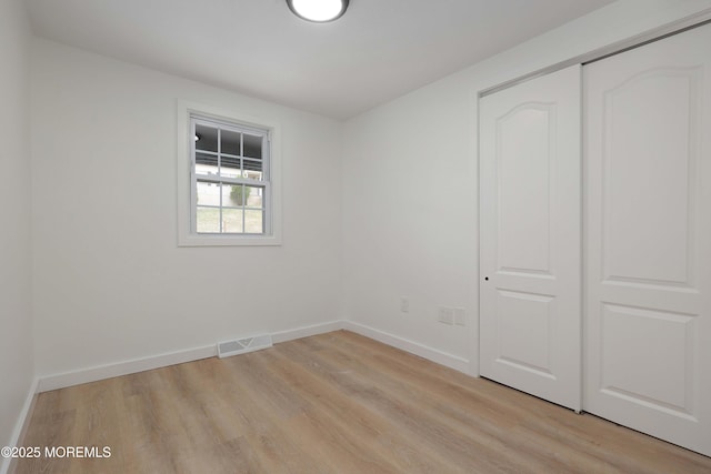 unfurnished bedroom with a closet, light wood-style floors, visible vents, and baseboards