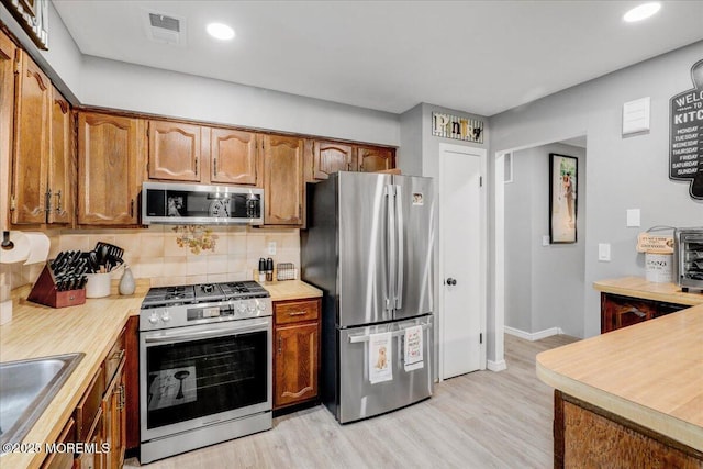 kitchen with a sink, stainless steel appliances, light wood finished floors, backsplash, and light countertops