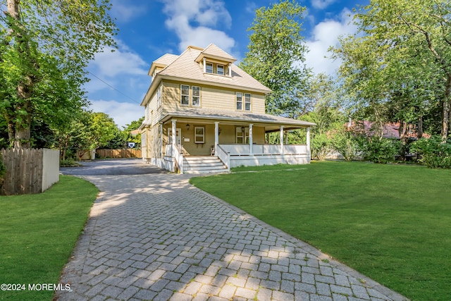 view of front of house featuring a front lawn, covered porch, fence, and decorative driveway