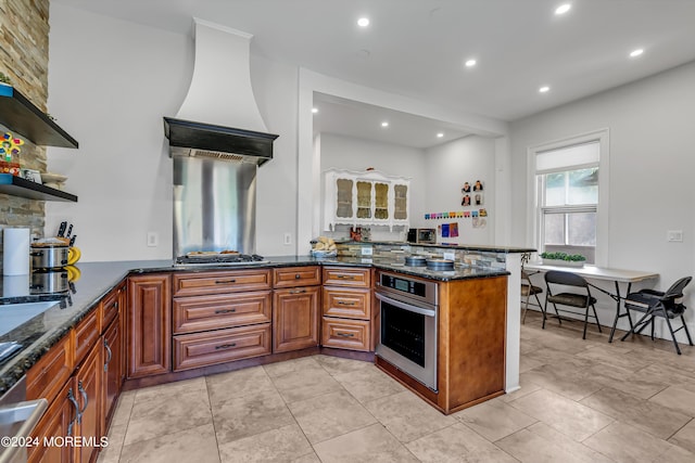 kitchen with recessed lighting, brown cabinetry, open shelves, dark stone counters, and oven