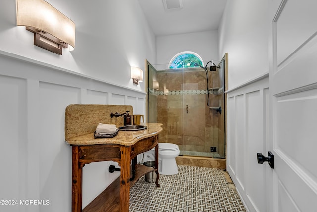 full bathroom featuring a sink, toilet, a decorative wall, a shower stall, and wainscoting