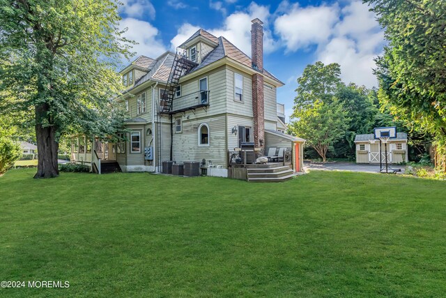 rear view of house featuring a chimney, an outbuilding, a wooden deck, and a lawn