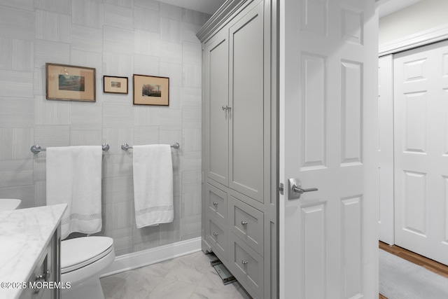bathroom featuring toilet, vanity, marble look tiles, and a tile shower
