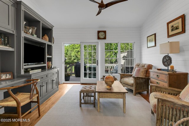 living area featuring ceiling fan, light wood finished floors, and wooden walls