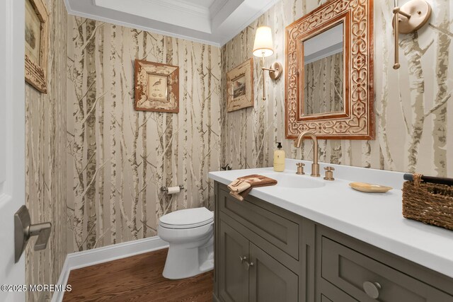 half bathroom featuring crown molding, wood finished floors, wallpapered walls, toilet, and vanity