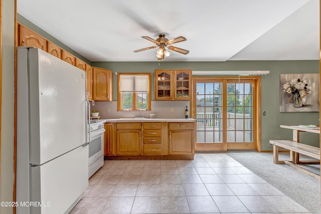 kitchen with white appliances, a ceiling fan, light countertops, a sink, and glass insert cabinets