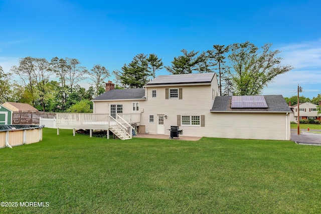rear view of house featuring solar panels, a chimney, a wooden deck, a yard, and a patio area
