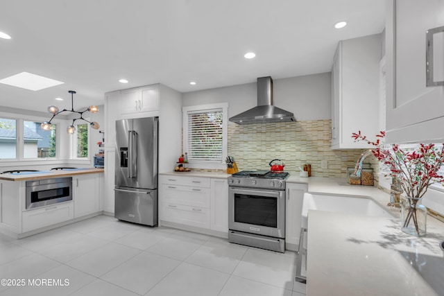 kitchen with wall chimney range hood, appliances with stainless steel finishes, a skylight, light countertops, and decorative backsplash