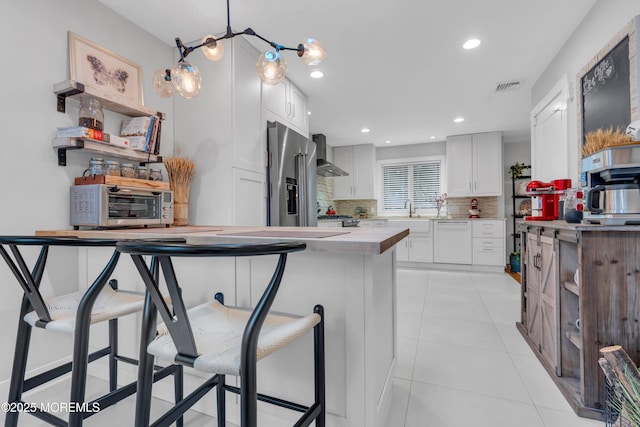 kitchen featuring high end refrigerator, wall chimney exhaust hood, a breakfast bar, backsplash, and white cabinetry