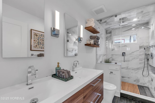bathroom featuring a marble finish shower, toilet, and double vanity