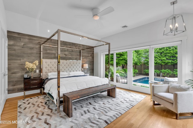 bedroom with multiple windows, wood walls, wood finished floors, a chandelier, and vaulted ceiling