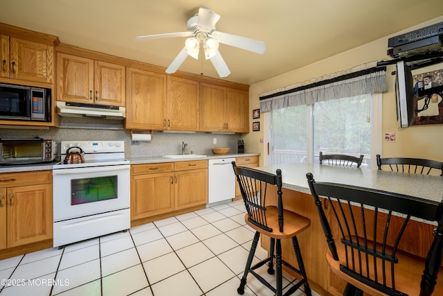 kitchen featuring white appliances, a sink, light countertops, and a kitchen bar