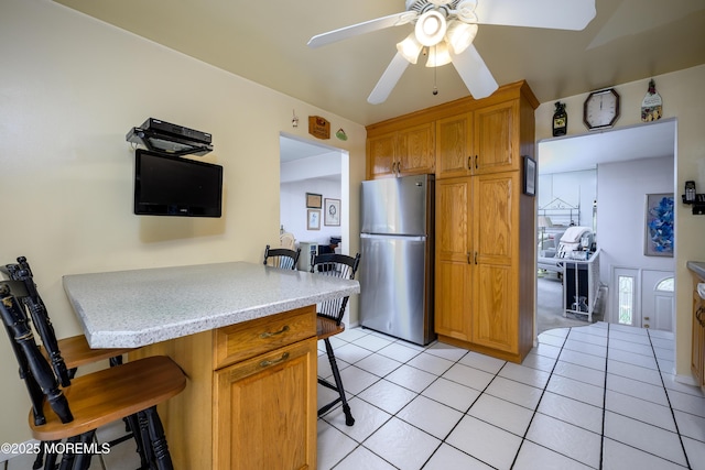 kitchen with freestanding refrigerator, a kitchen bar, a ceiling fan, light tile patterned floors, and light countertops